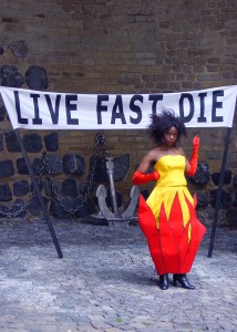 Outfit #1, (Fireball dress), 2009 / handmade, linen, cotton, chintz, red satin gloves & LIVEFASTDIE, 2009 / ca 200 x 40 cm, handprinted lettering on canvas, wooden poles